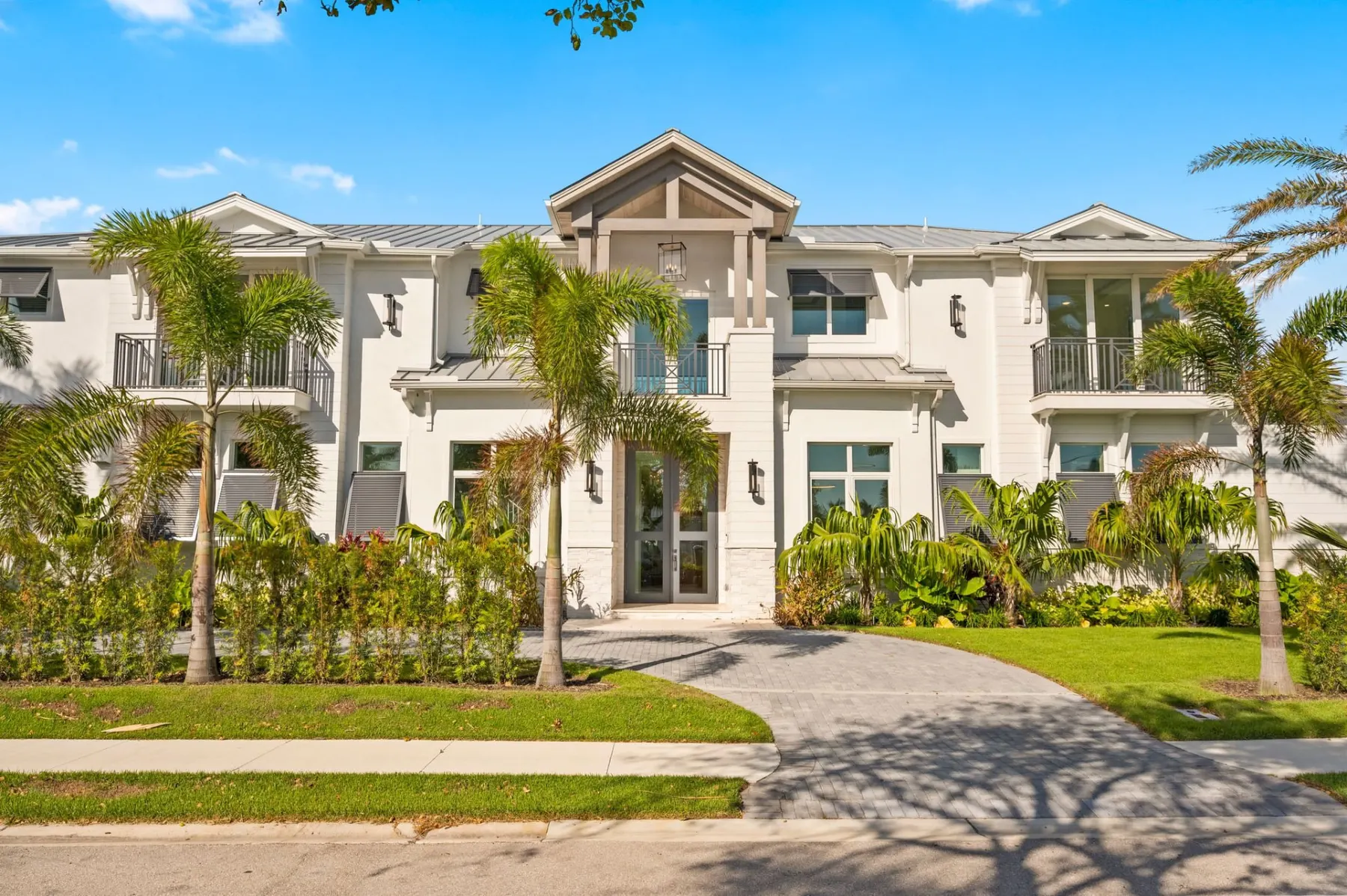 Front of the home straight on, with a gabled entry, second-floor balconies with crossed railings and a paver driveway curving to the door.