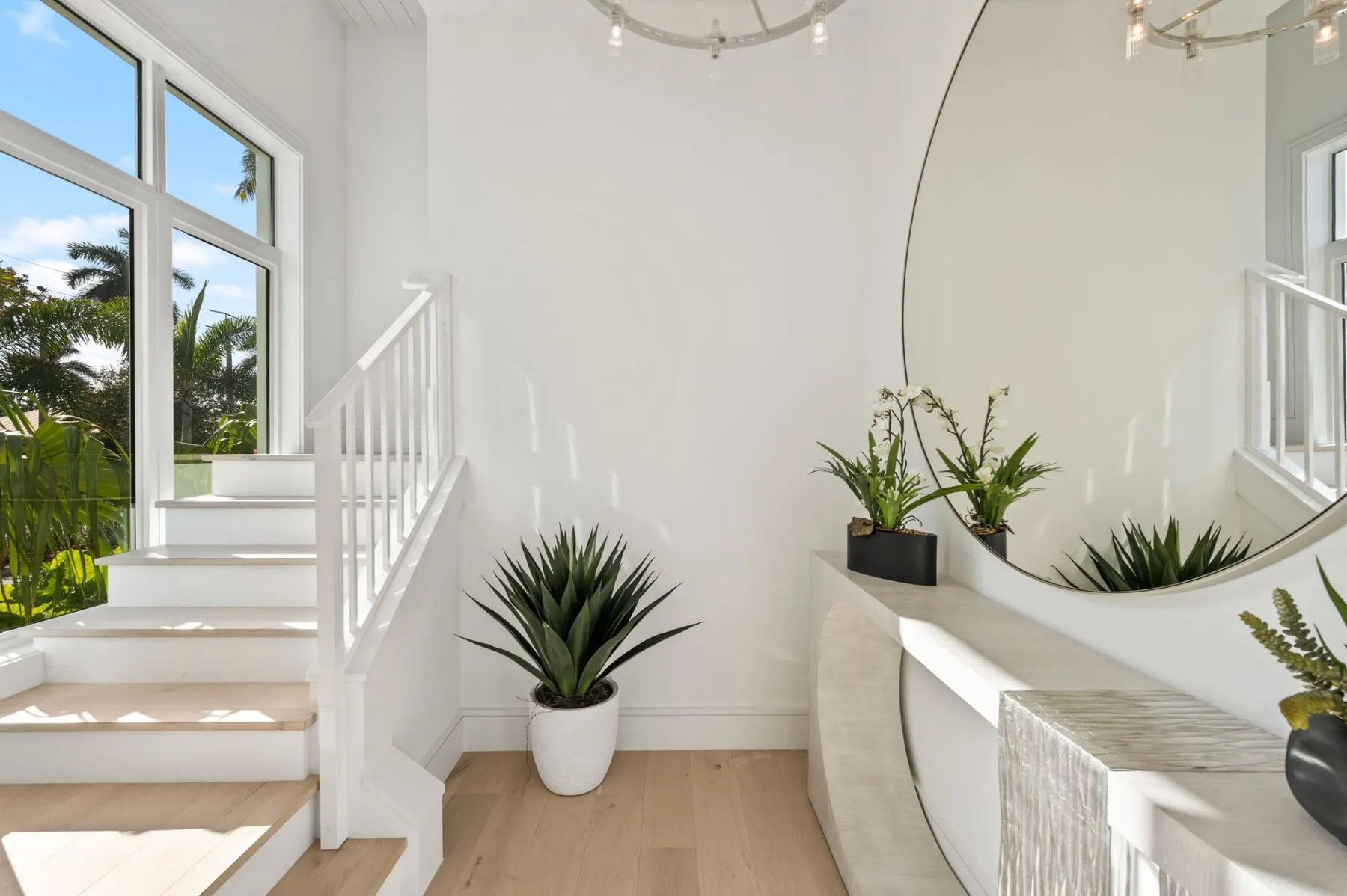 Stair landing with a tall window, a white railing, a round mirror and a console table.