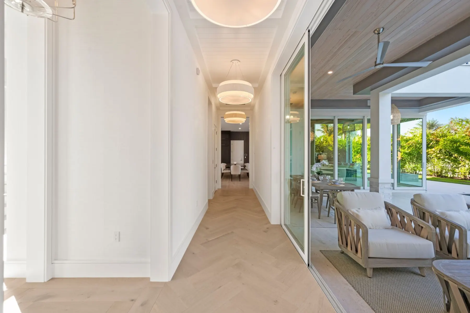 Hallway with herringbone wood floors and round pendants, opening to the covered lanai through sliding glass doors.