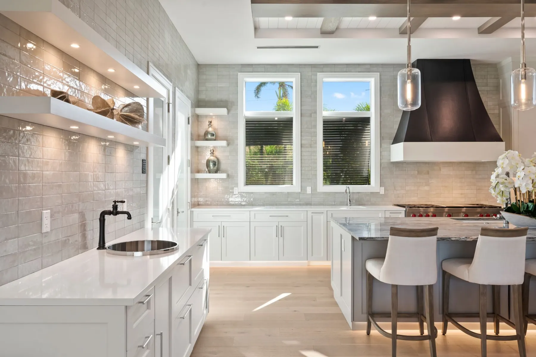 Kitchen with a glazed tile wall, floating shelves, a round bar sink, a black hood and a stone-top island.