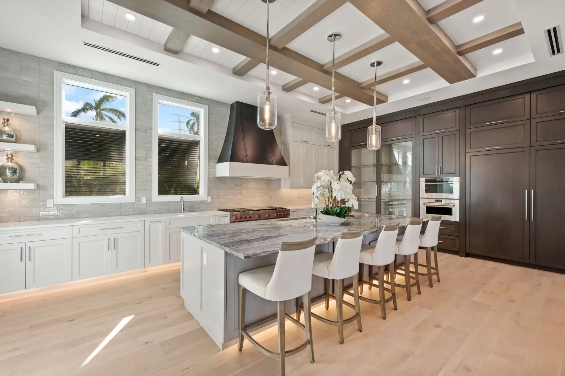 Kitchen island with five counter stools, glass pendants, a black range hood and dark built-in cabinets.