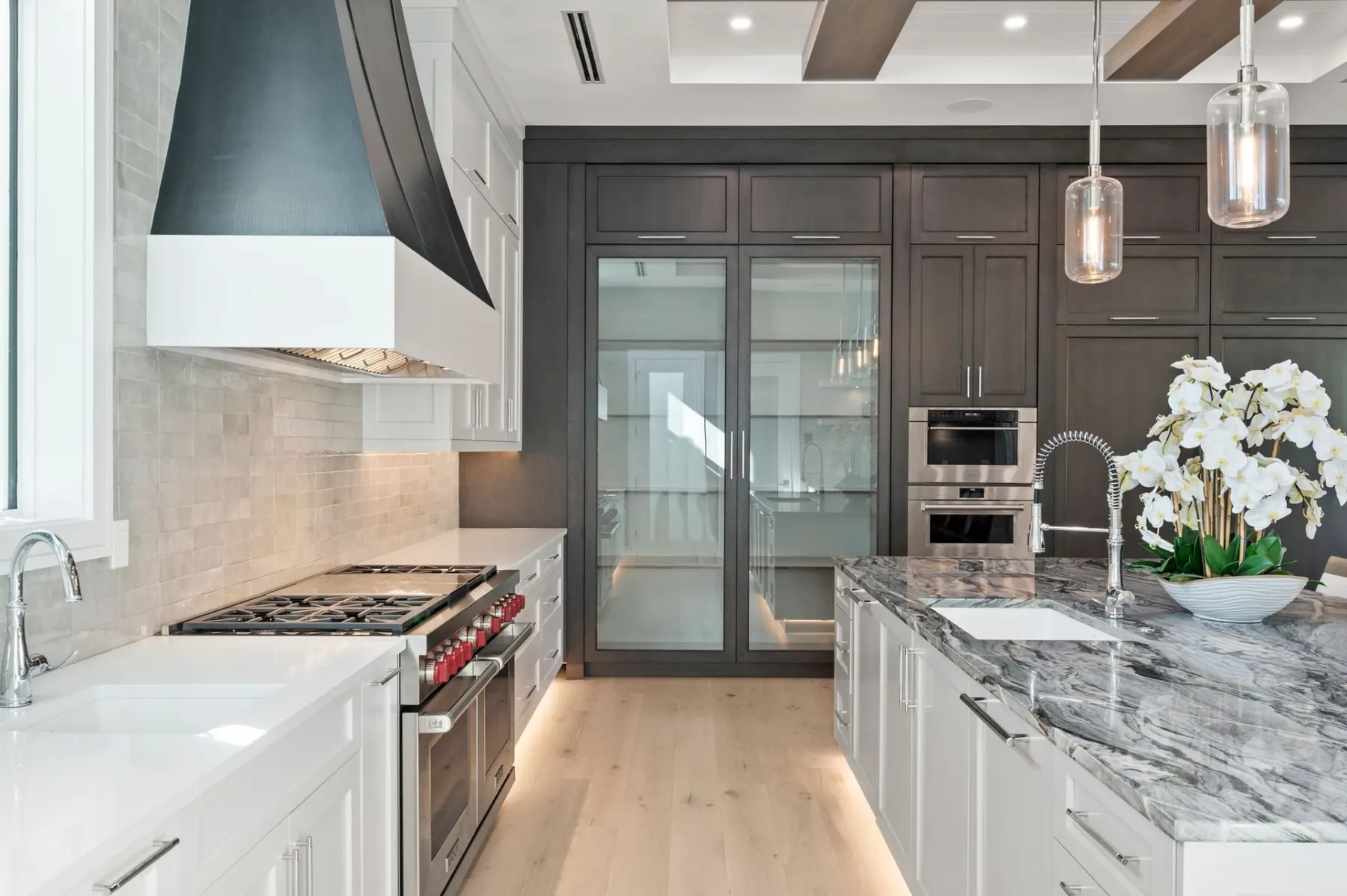 Close view of the gas range, glass-front cabinets, stainless steel ovens and a stone-top island.