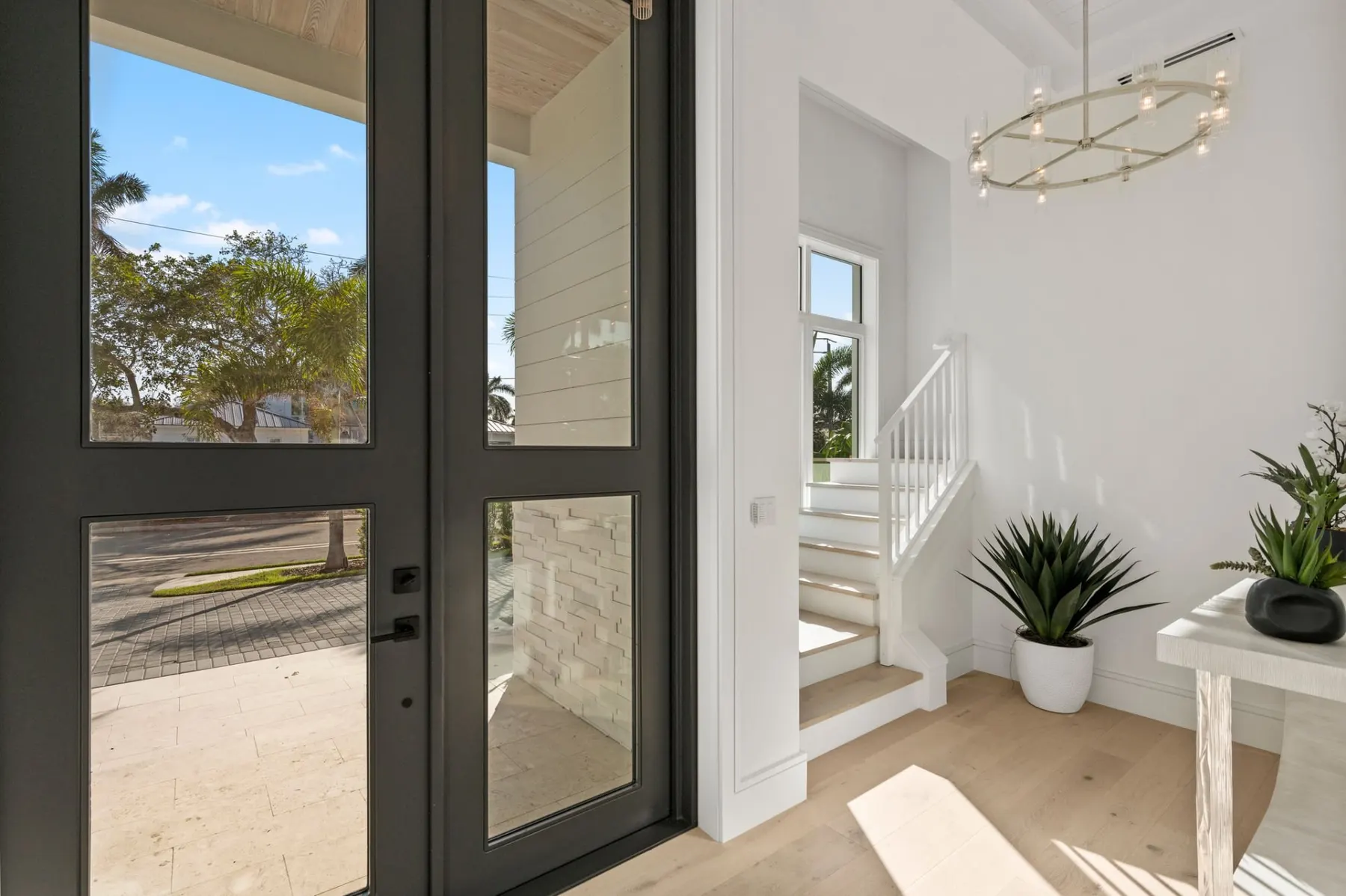 Front door and stair beyond the foyer, with a ring chandelier, a white railing and wood treads.
