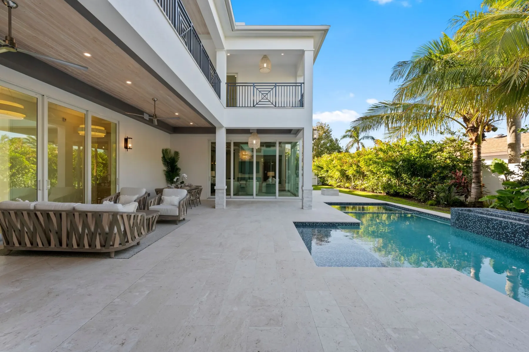 Covered terrace with outdoor sofas beside the pool, with a two-story balcony above.