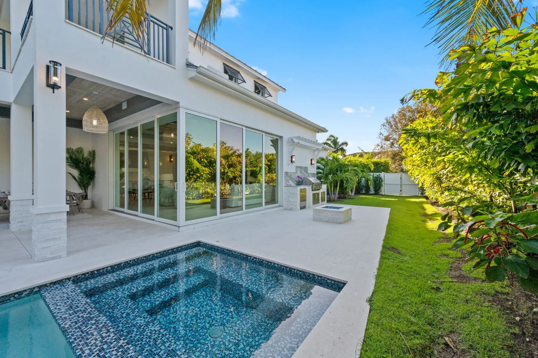 Spa with blue mosaic tile and the pool, with an outdoor kitchen and fire pit on the paver terrace.
