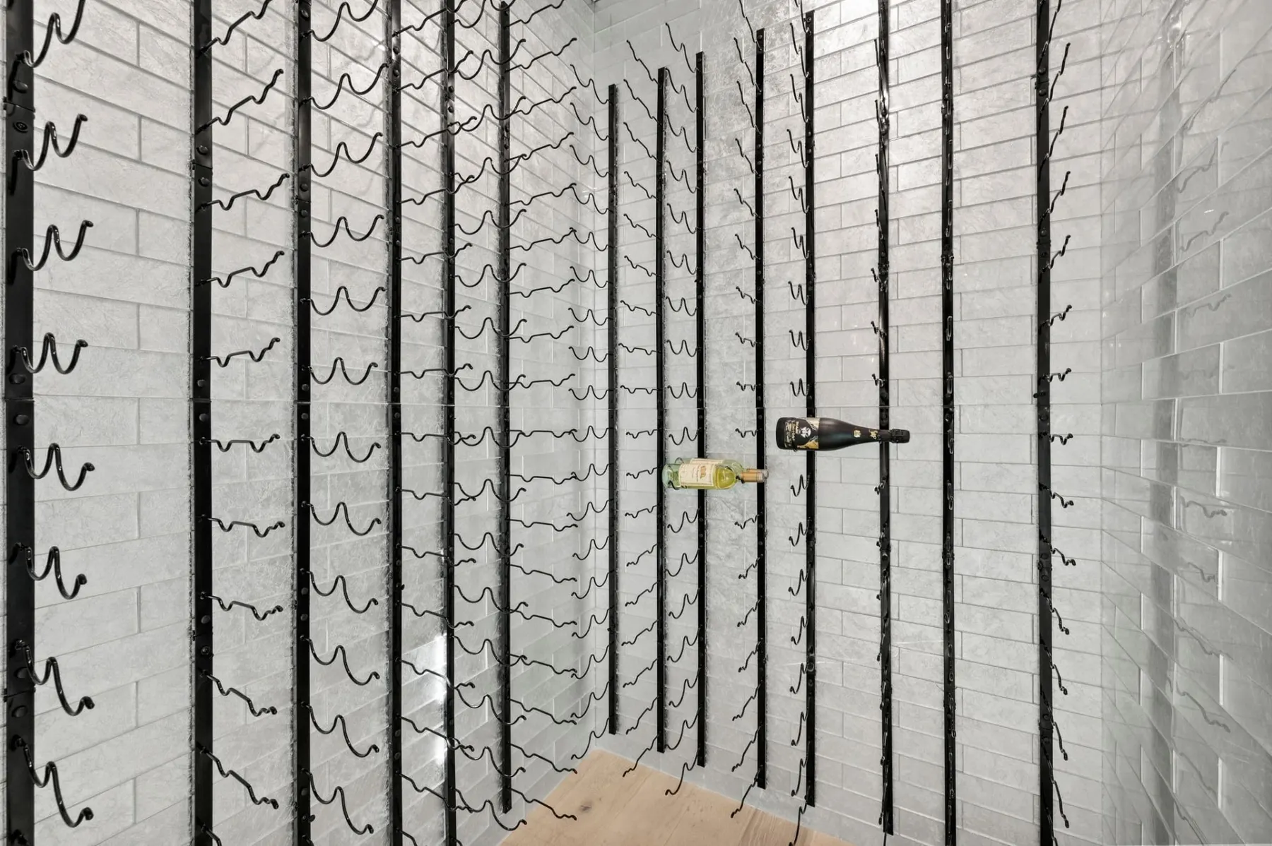 Wine room with wall-mounted black racks on light tile walls.