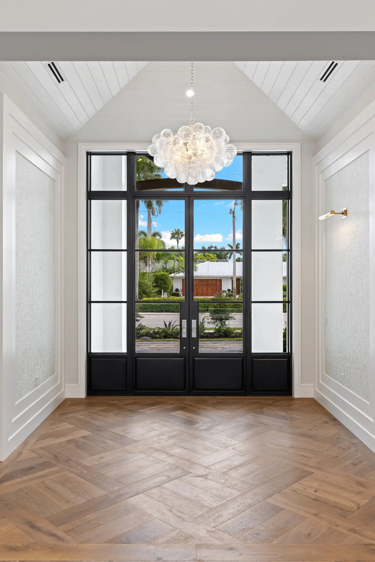 Foyer with black-framed glass double doors, a glass-globe cluster chandelier and a herringbone wood floor.