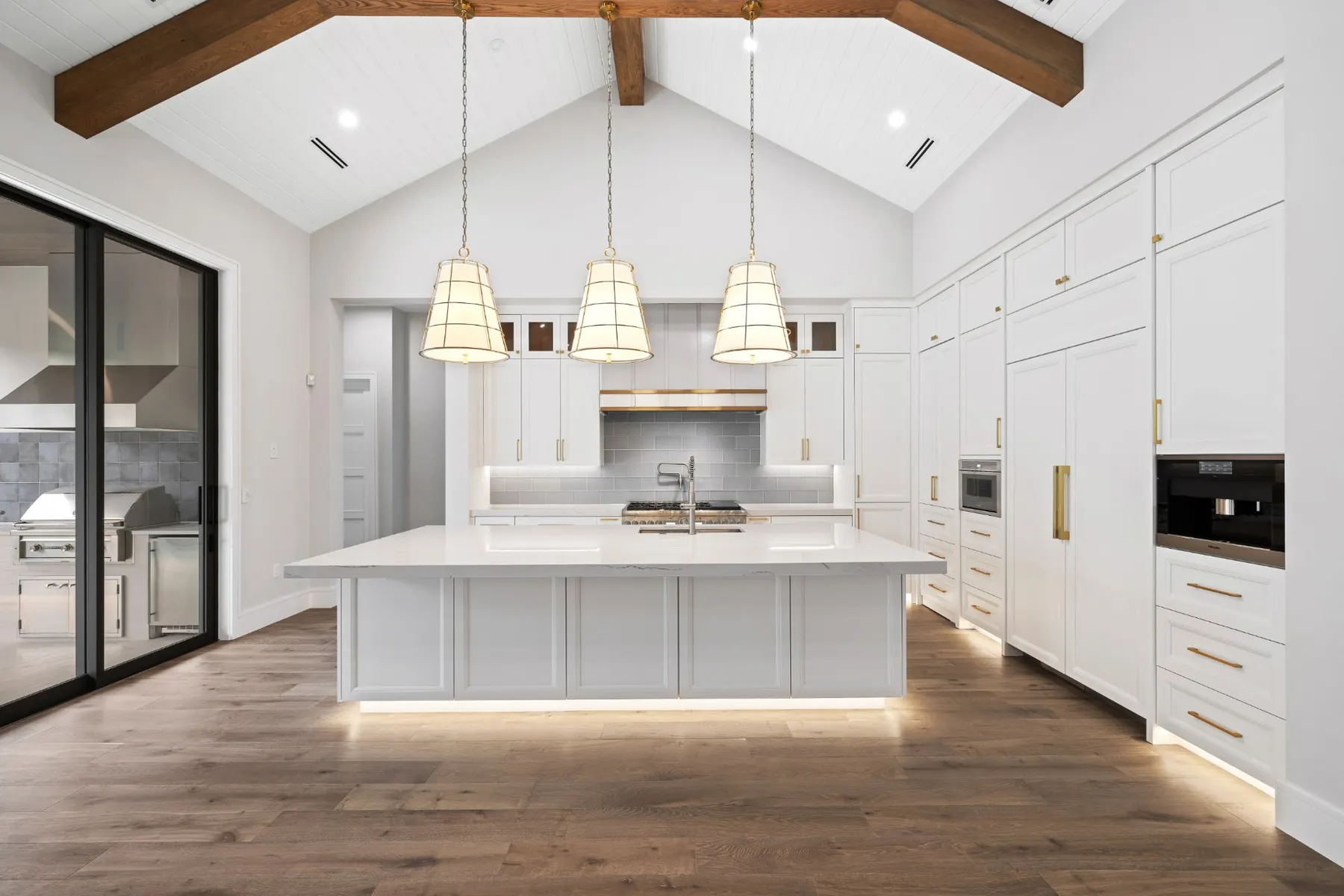 Kitchen with a long white island, three woven pendants and a vaulted ceiling with timber trusses.