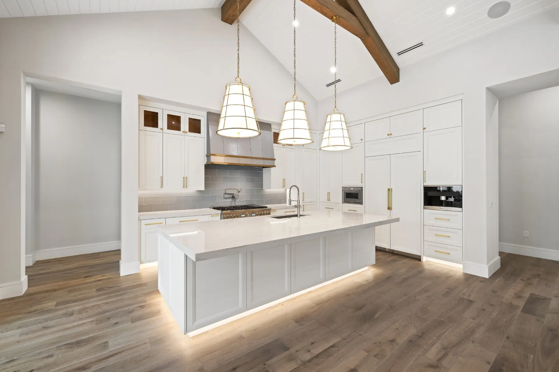Kitchen from the side showing the island, range hood and a wall of white cabinets with built-in ovens.