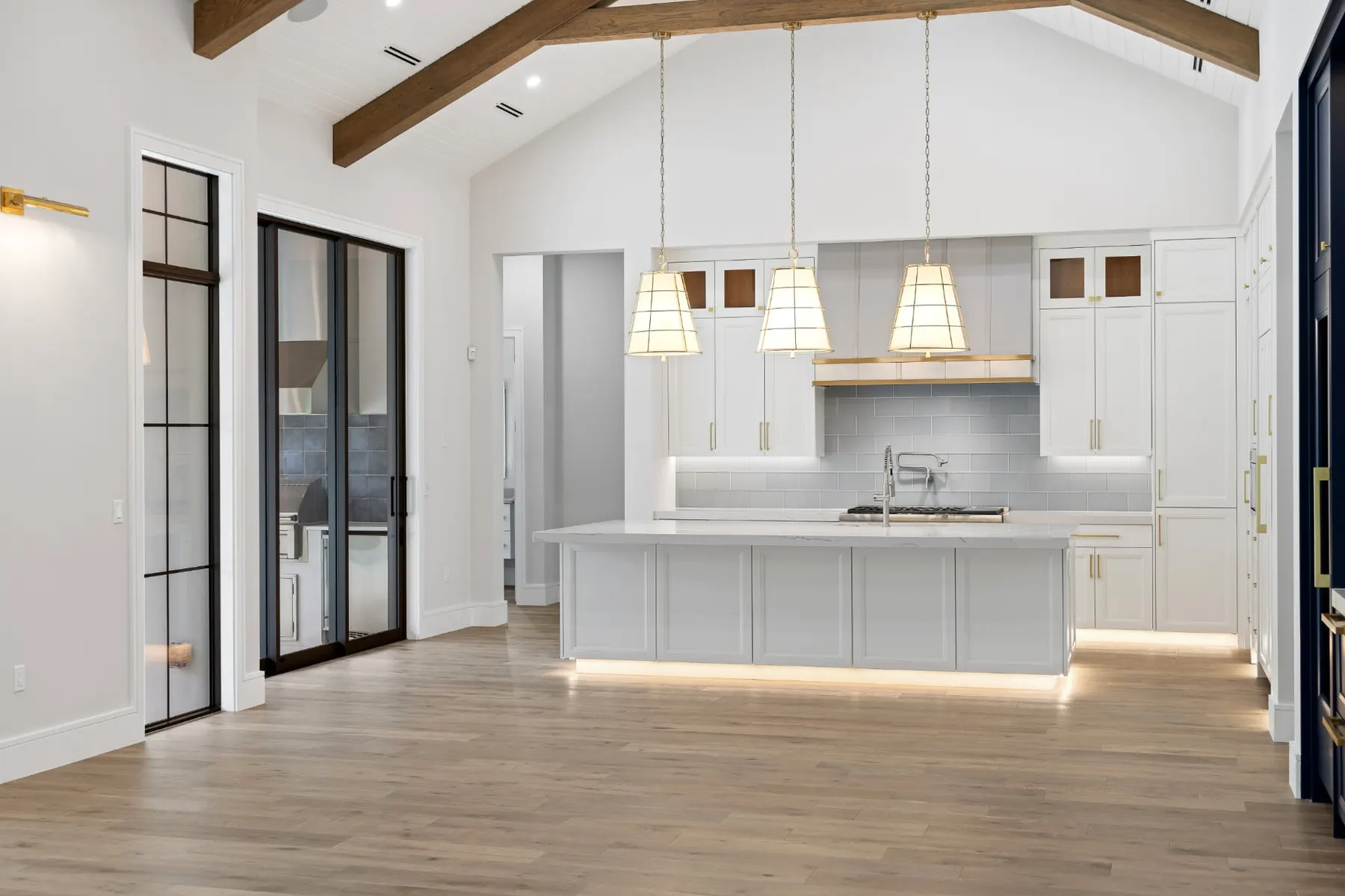 Kitchen and island seen across the great room, with woven pendants and black-framed glass doors.
