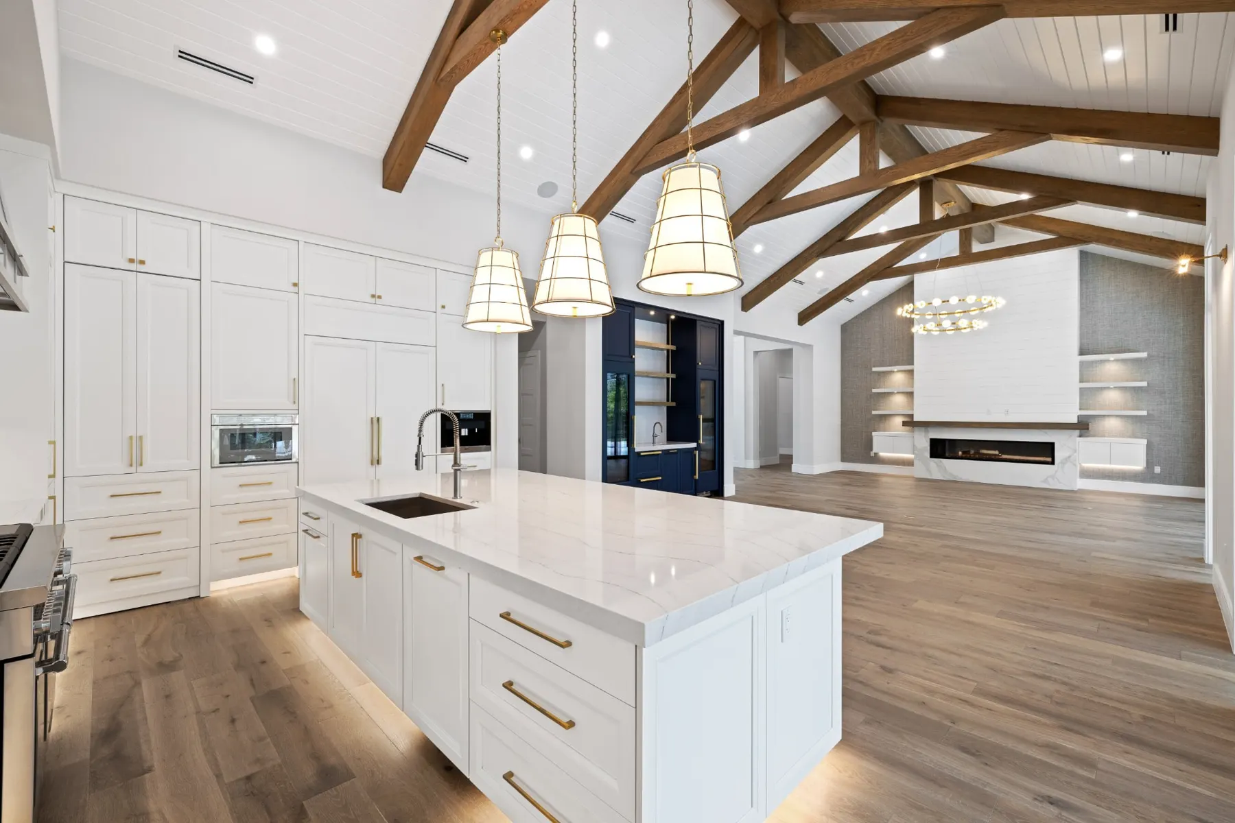 Kitchen island with brass pulls and a built-in oven wall, with the great room and fireplace beyond.