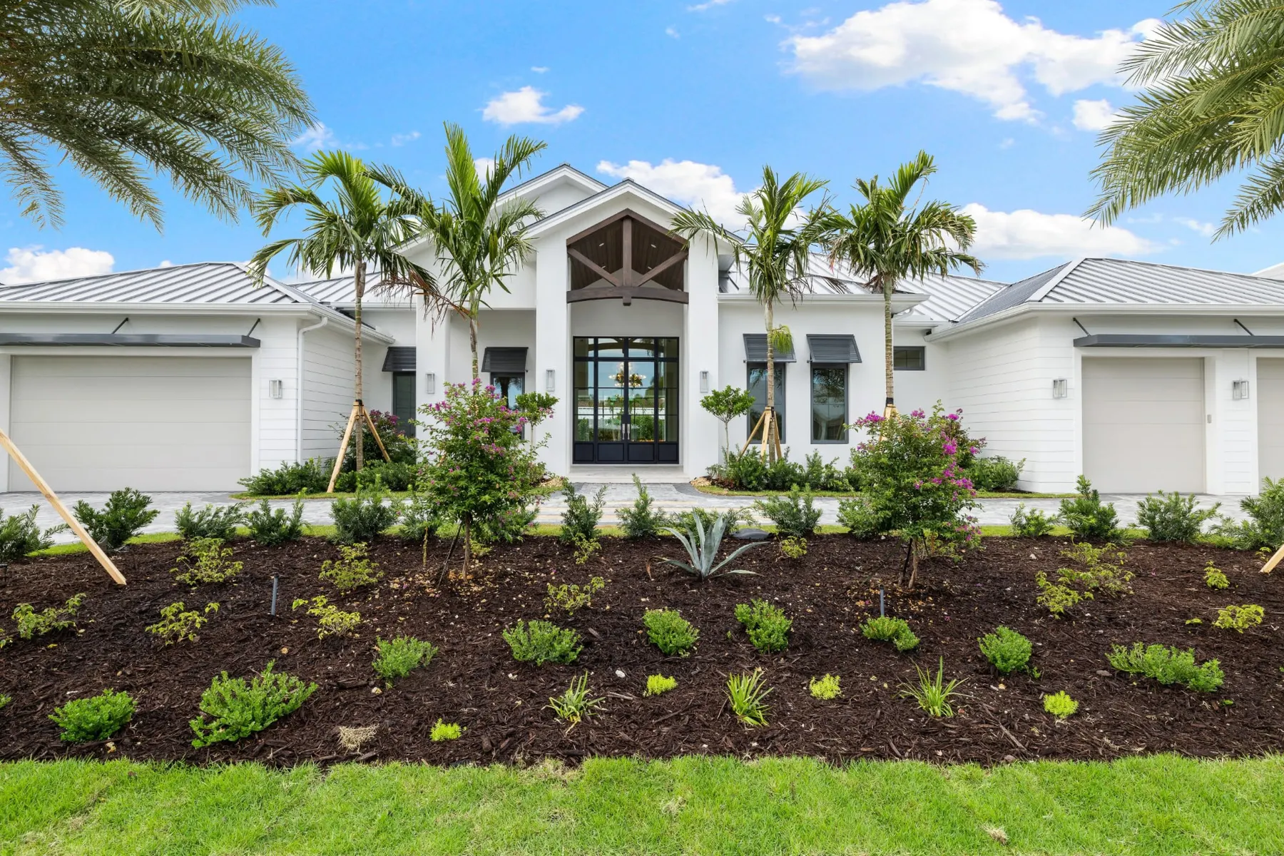 Front of the home in daylight, straight on, with the timber-trussed entry, glass double doors and a mulched planting bed.