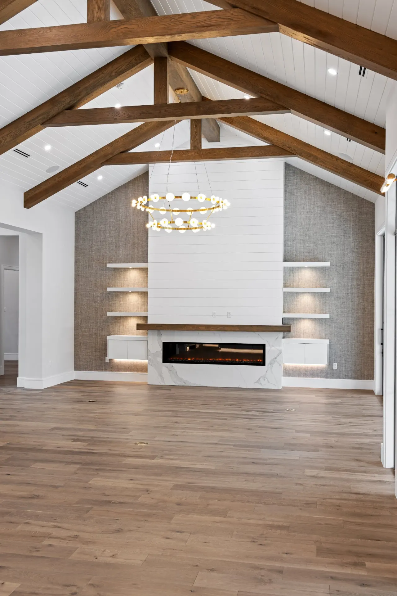 Portrait view of the shiplap fireplace wall with built-in shelves and a brass ring chandelier.