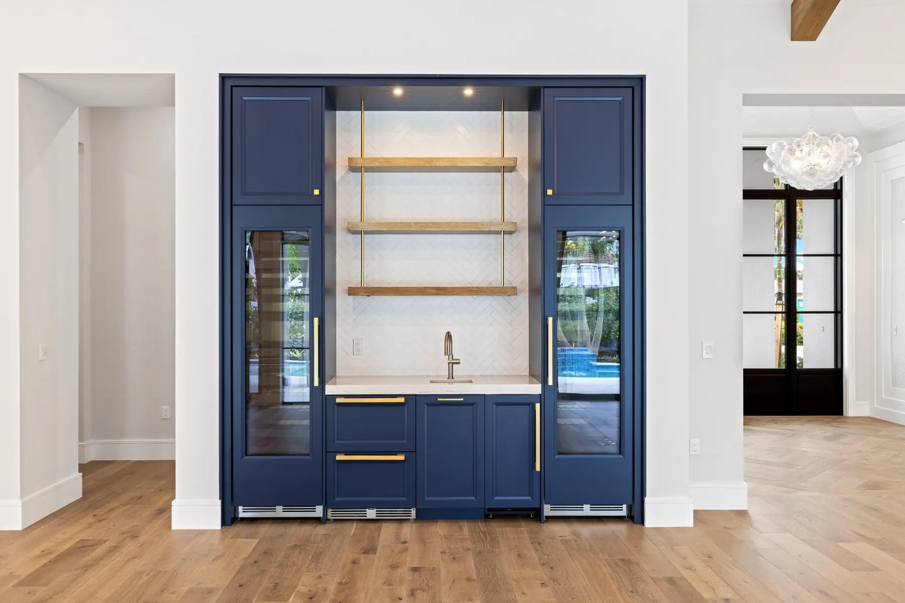 Navy bar with glass-front beverage coolers, open shelves and a sink set in a wall niche.
