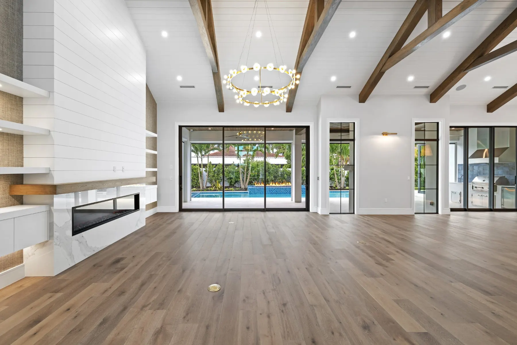 Great room with a shiplap fireplace wall, brass ring chandelier, timber beams and sliding glass doors to the pool.