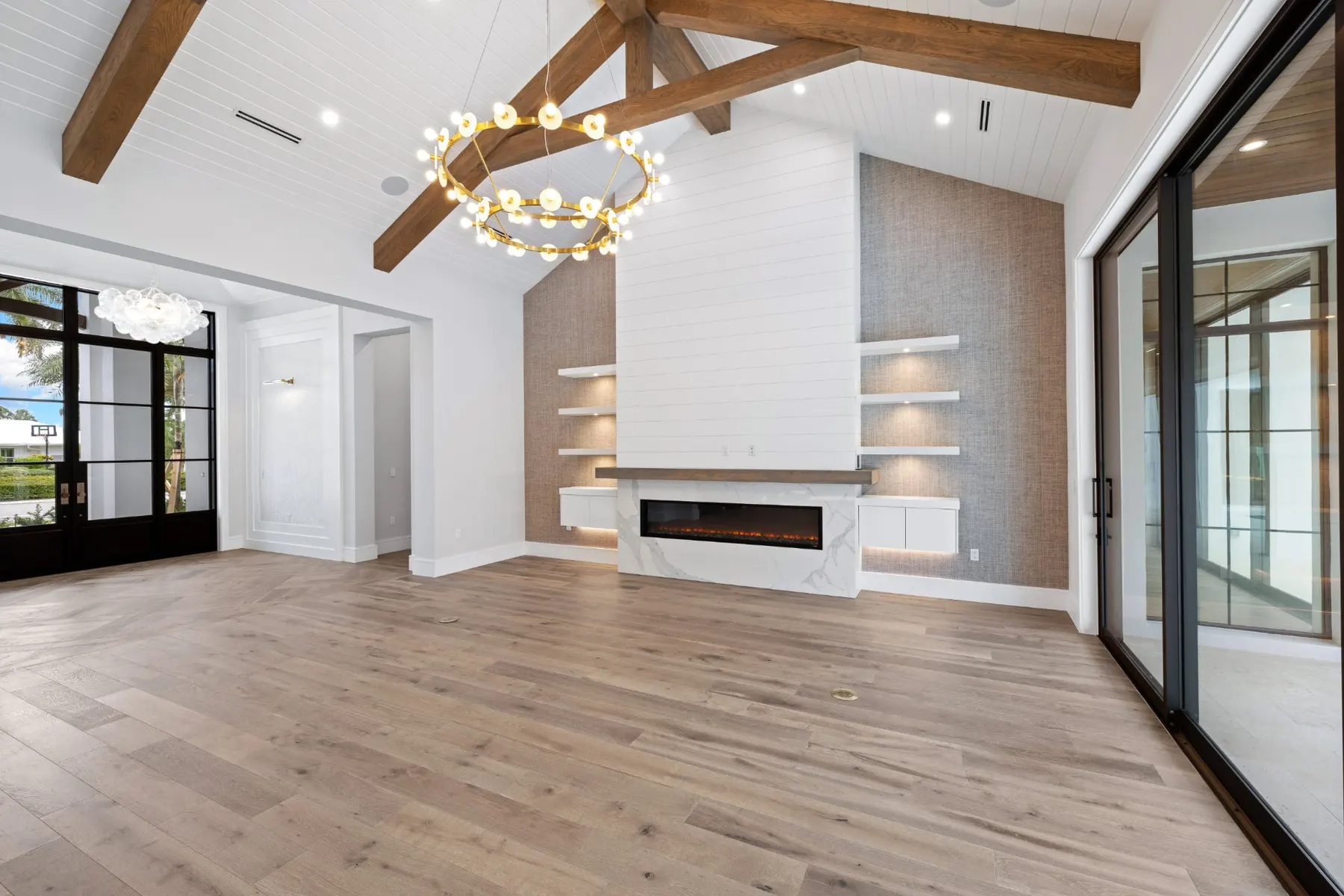 Great room fireplace wall with shiplap, built-in shelves and a brass ring chandelier beneath timber trusses.