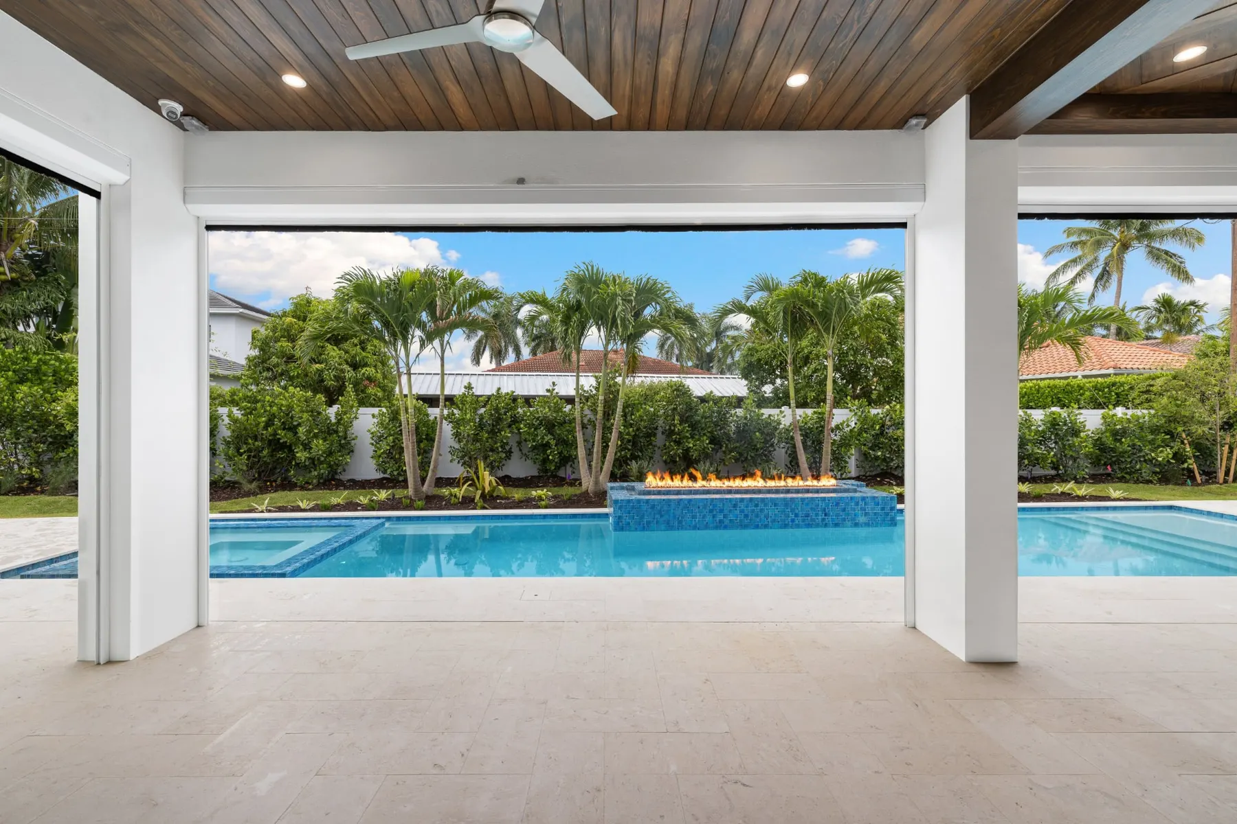 Covered lanai with a stained wood ceiling and ceiling fan, looking out to the pool and fire feature.