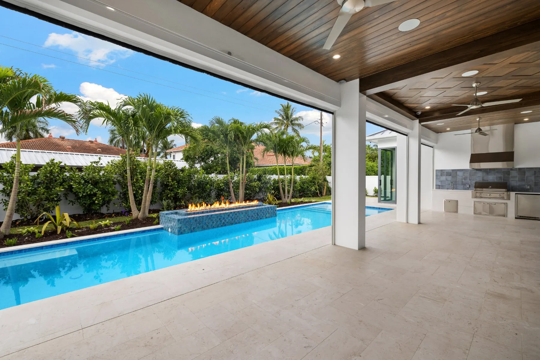 Lanai and pool in daylight with a raised fire feature and the outdoor kitchen beyond.