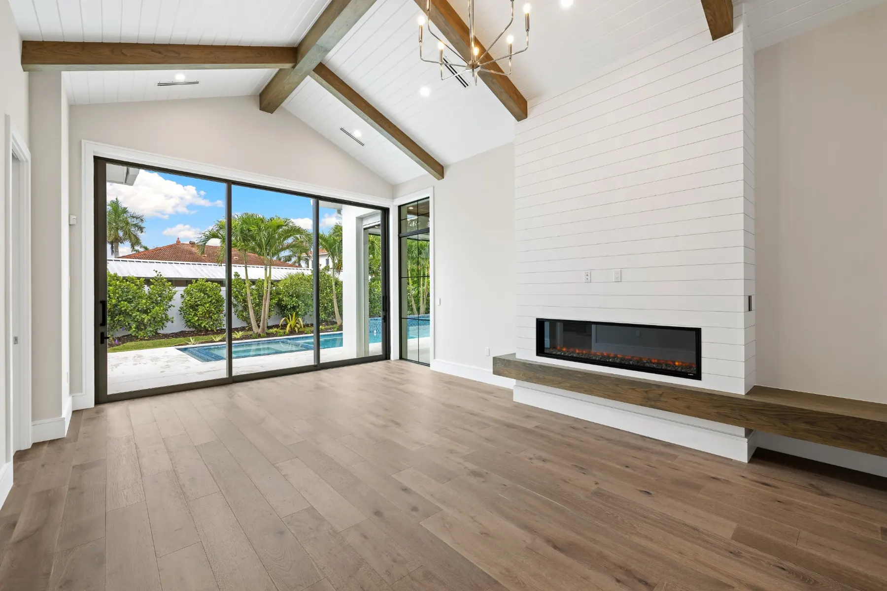 Living room with a long linear fireplace, a wood-top hearth and sliding glass doors to the pool.