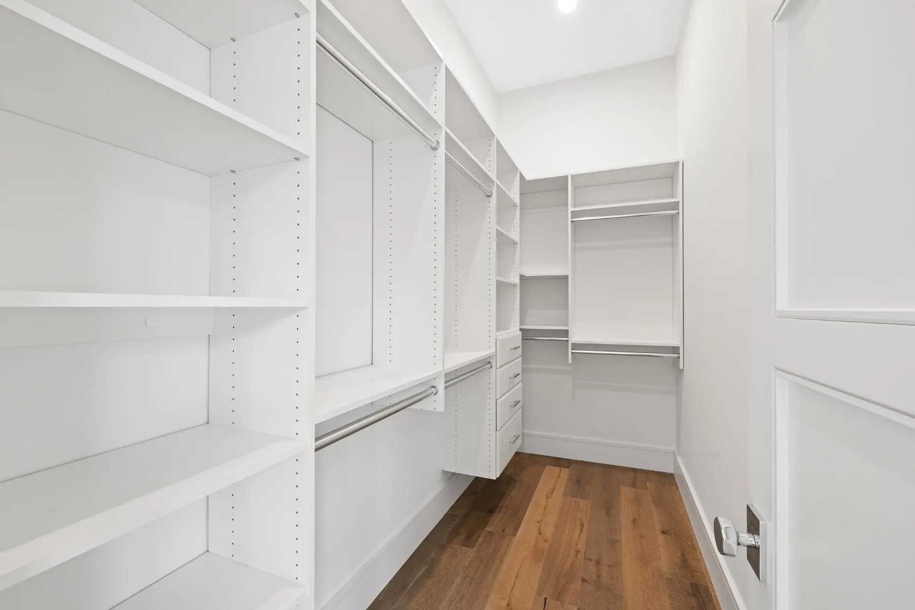 Second walk-in closet with white shelving, hanging rods and drawers.