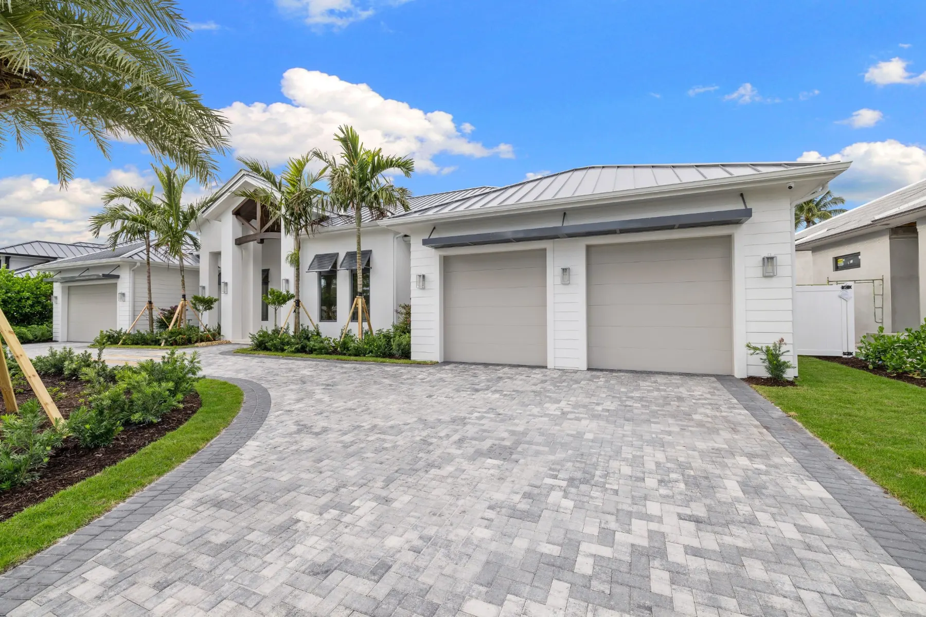 Front of the home in daylight with a two-car garage, bahama-style shutters, a curved paver driveway and the entry gable.