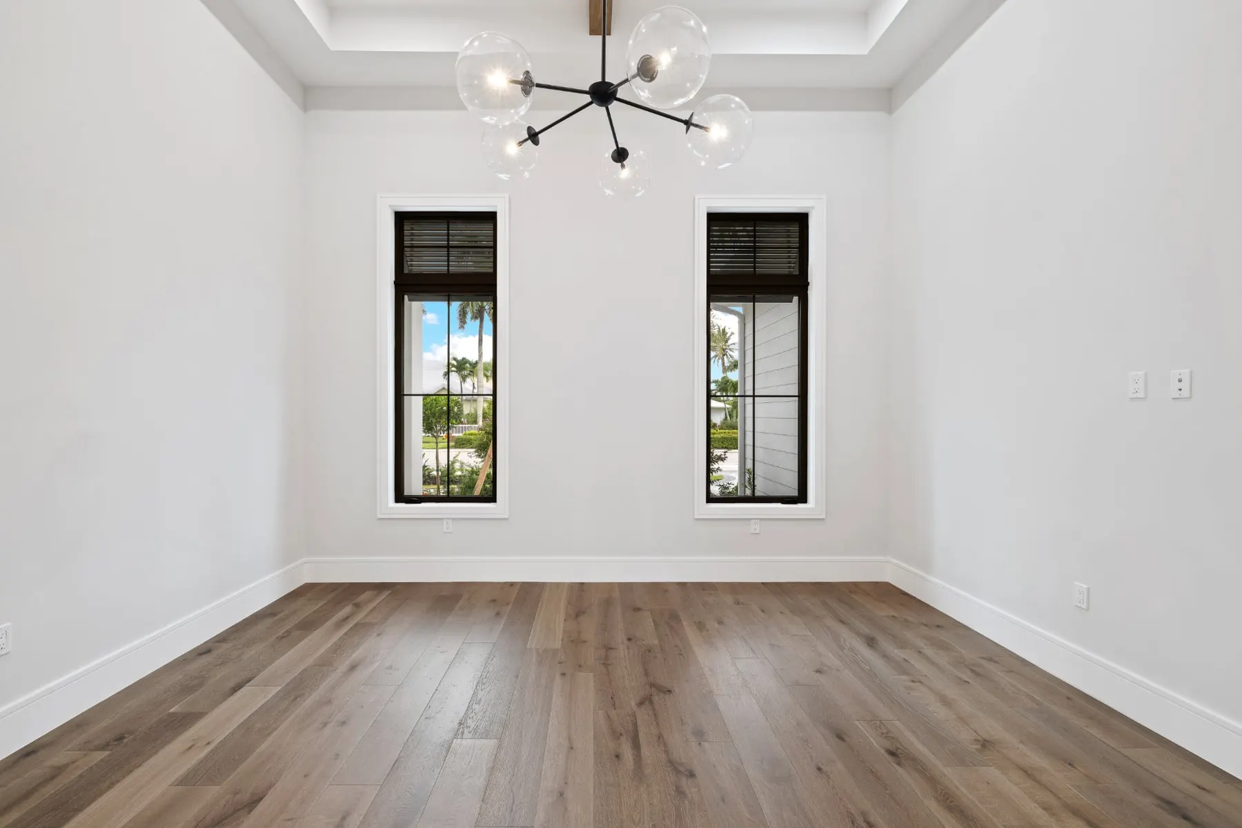 Empty front room with a globe chandelier, a tray ceiling and two tall windows.