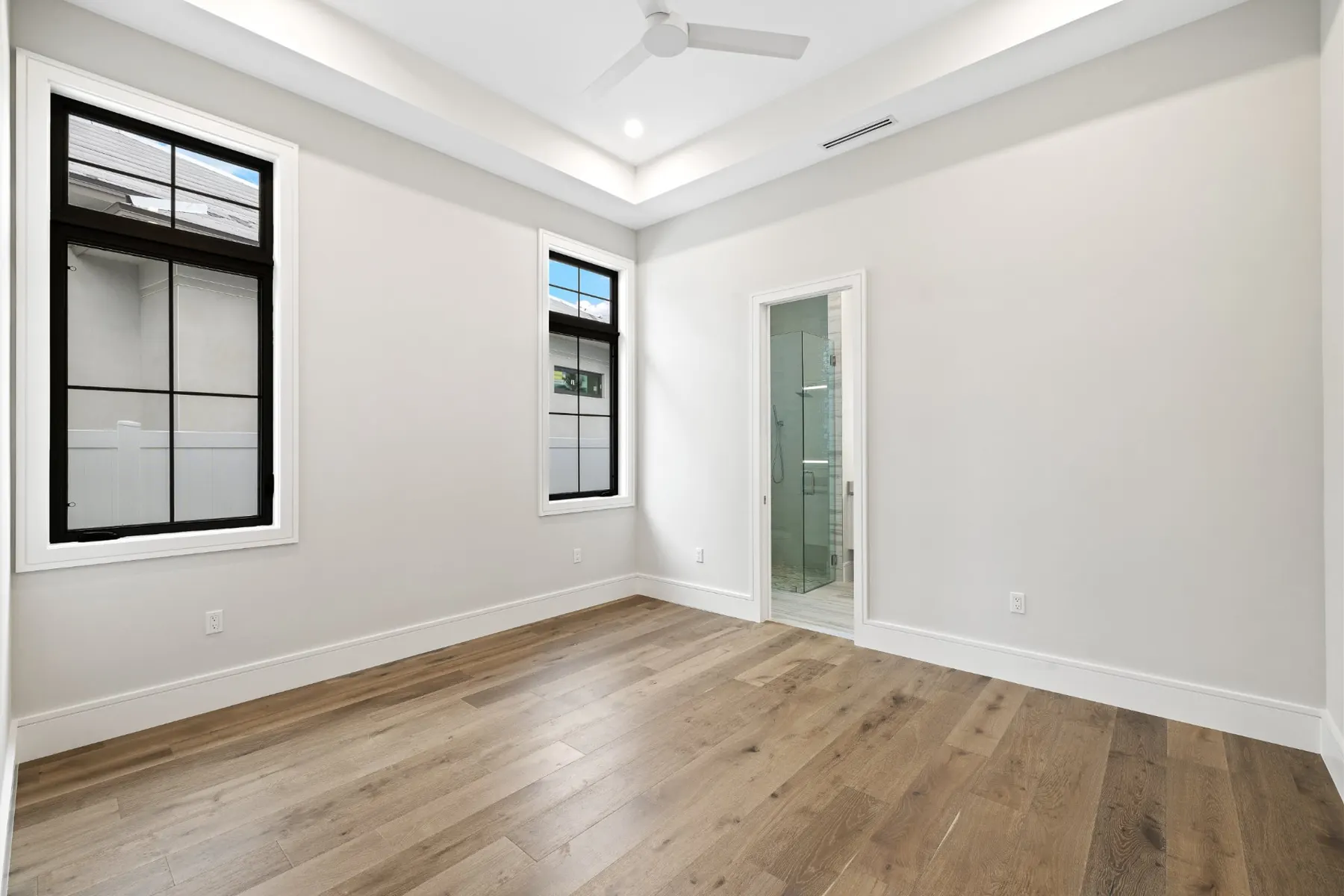 Bedroom with a tray ceiling, ceiling fan, black-framed windows and a bath doorway.