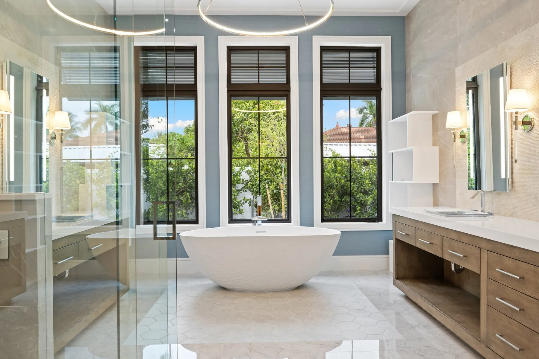 Bath with a freestanding tub centered under three windows, a wood vanity at right and the glass shower at left.