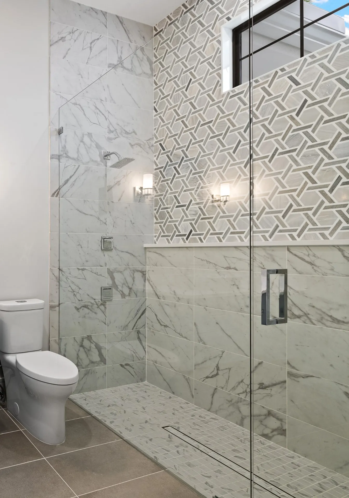 Portrait view of a shower with marble-look tile and a patterned mosaic accent wall.