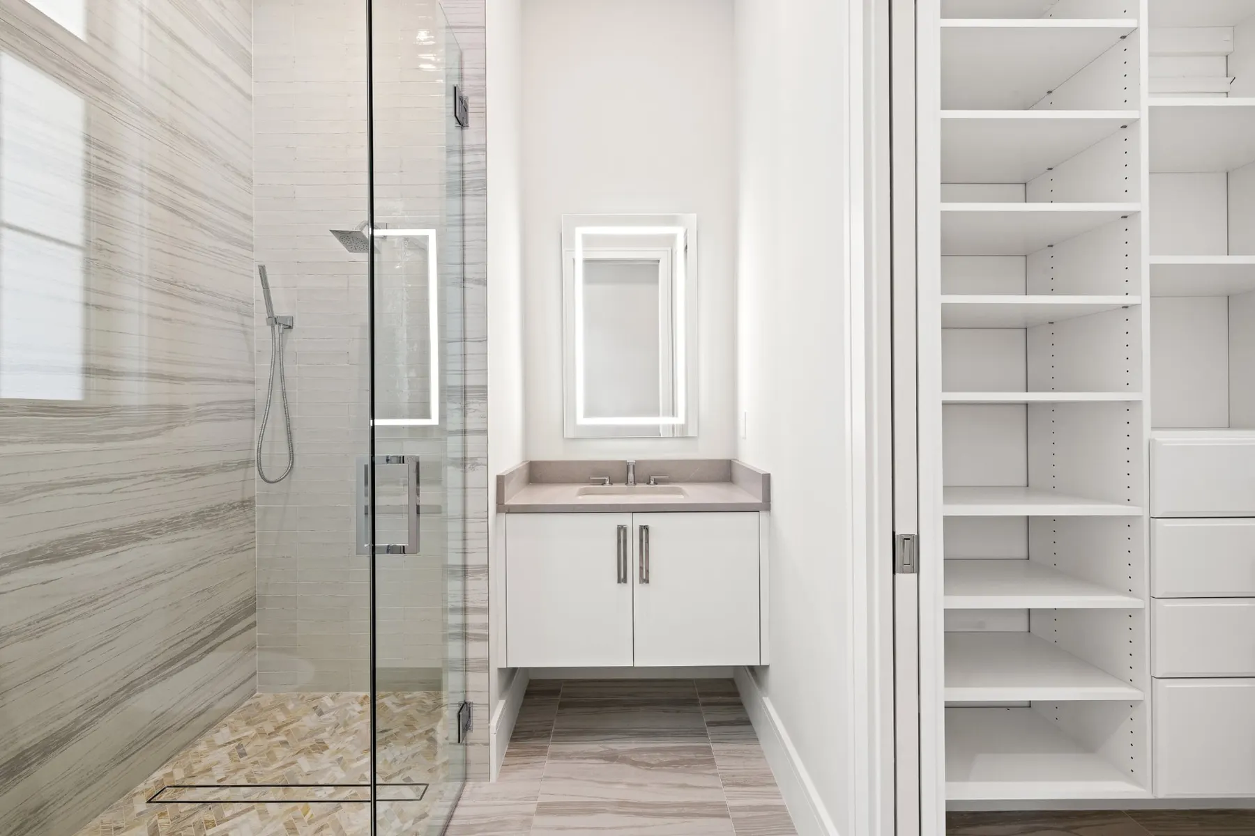 Bath with a floating white vanity, a lit mirror and a glass shower in striped tile, beside a closet.