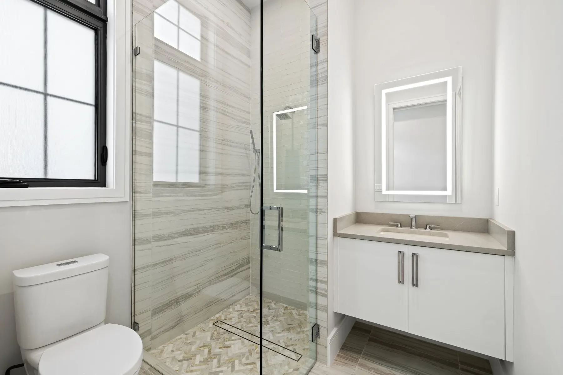 Bath with a glass-enclosed shower in striped tile, a toilet and a floating white vanity.