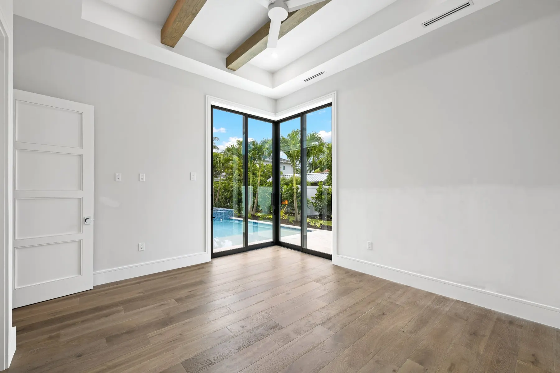 Bedroom with exposed wood beams, a corner of glass doors and a view of the pool.