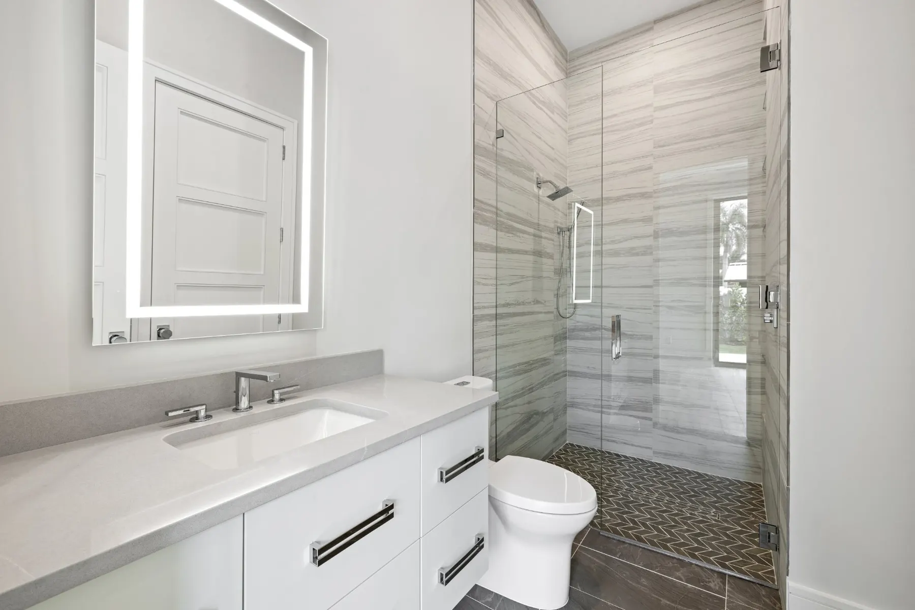 Bath with a floating vanity, a lit mirror and a frameless glass shower in striped tile.