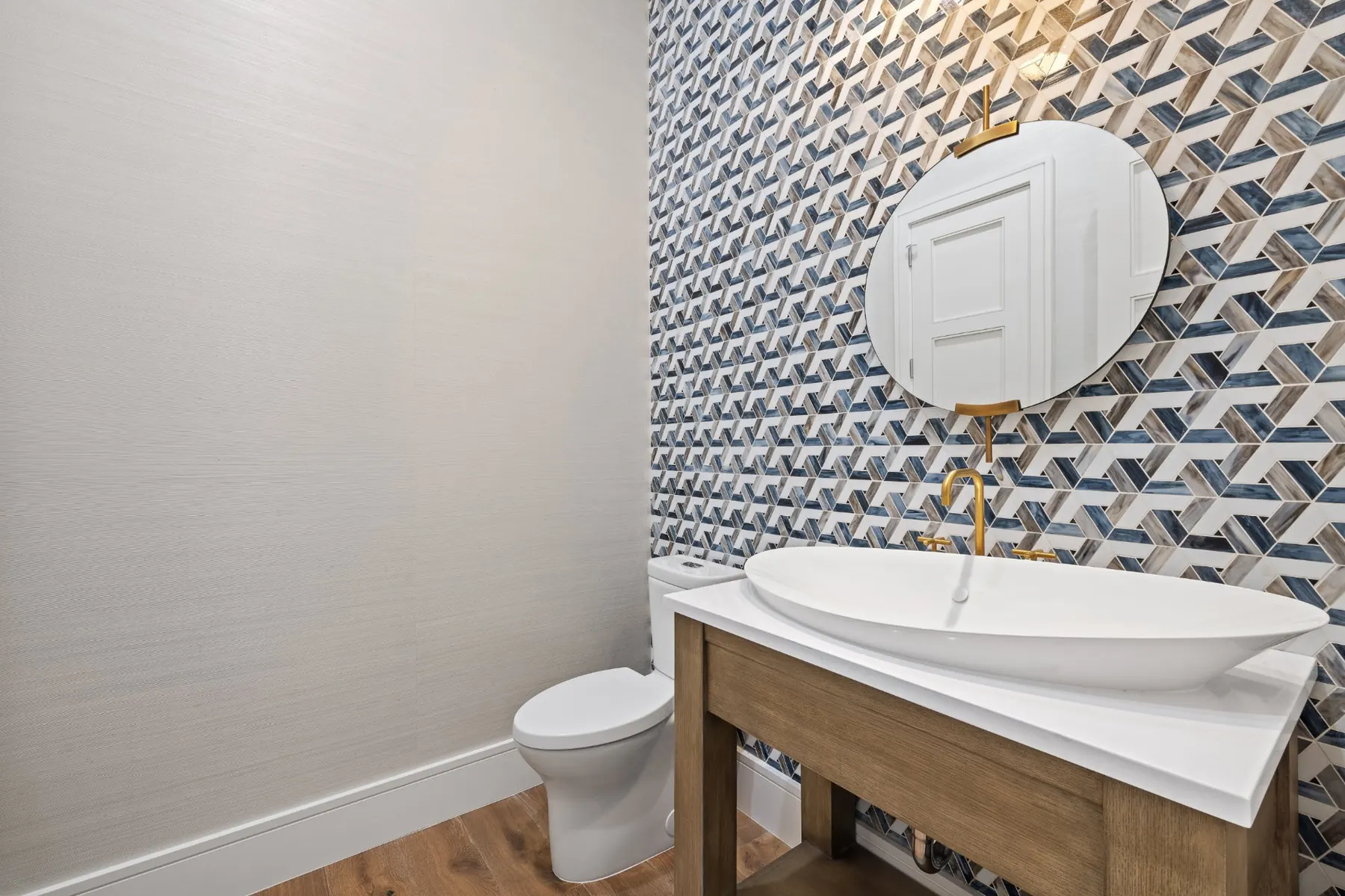 Powder room with a blue and tan mosaic accent wall, a round mirror, a vessel sink and brass fixtures.
