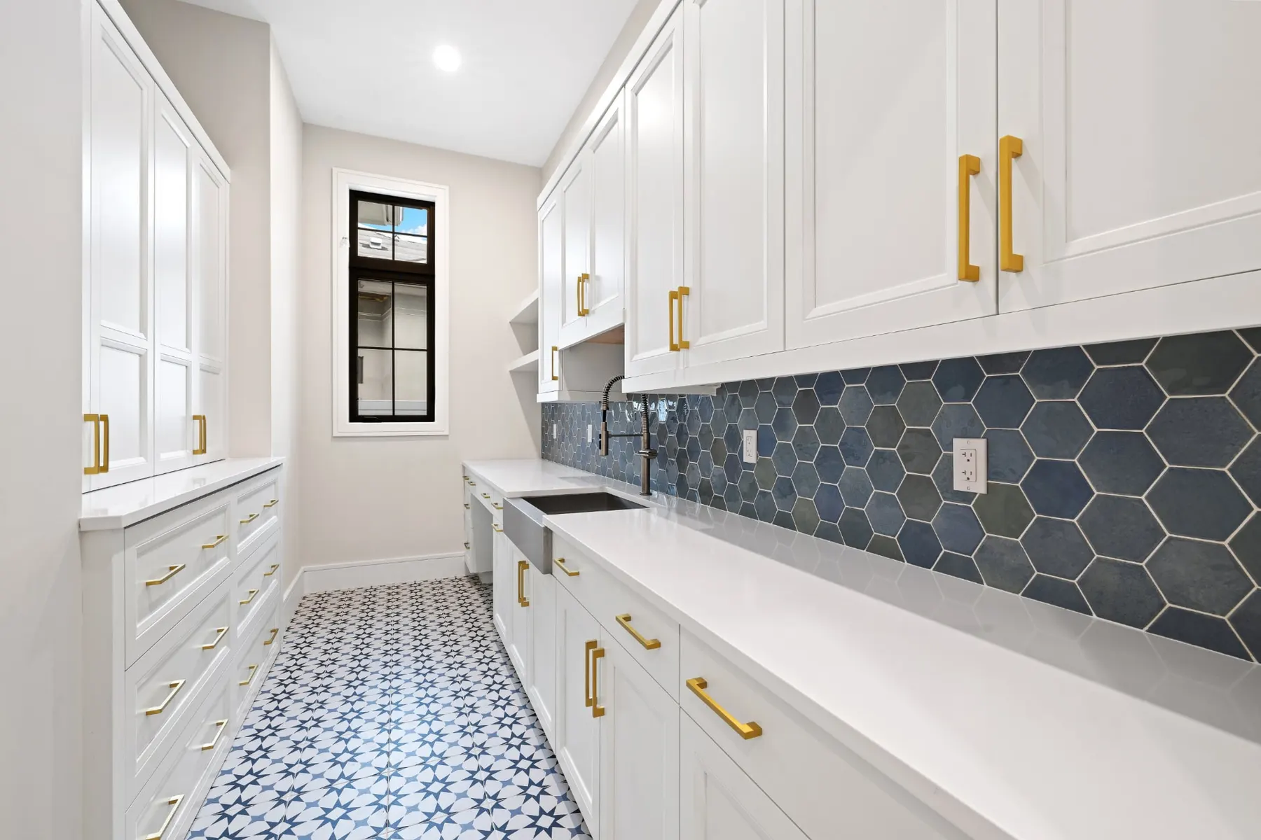 Utility room with white cabinets, brass pulls, a blue hex tile backsplash and patterned floor tile.