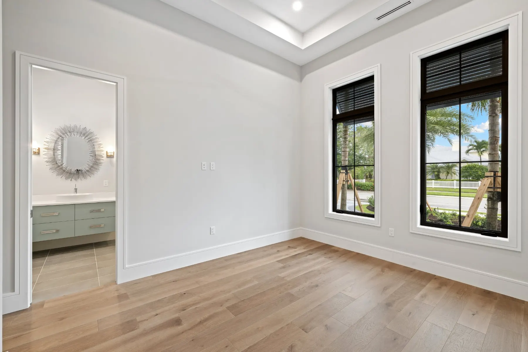 Bedroom with an adjoining bath seen through the doorway, with a sunburst mirror and a floating vanity.