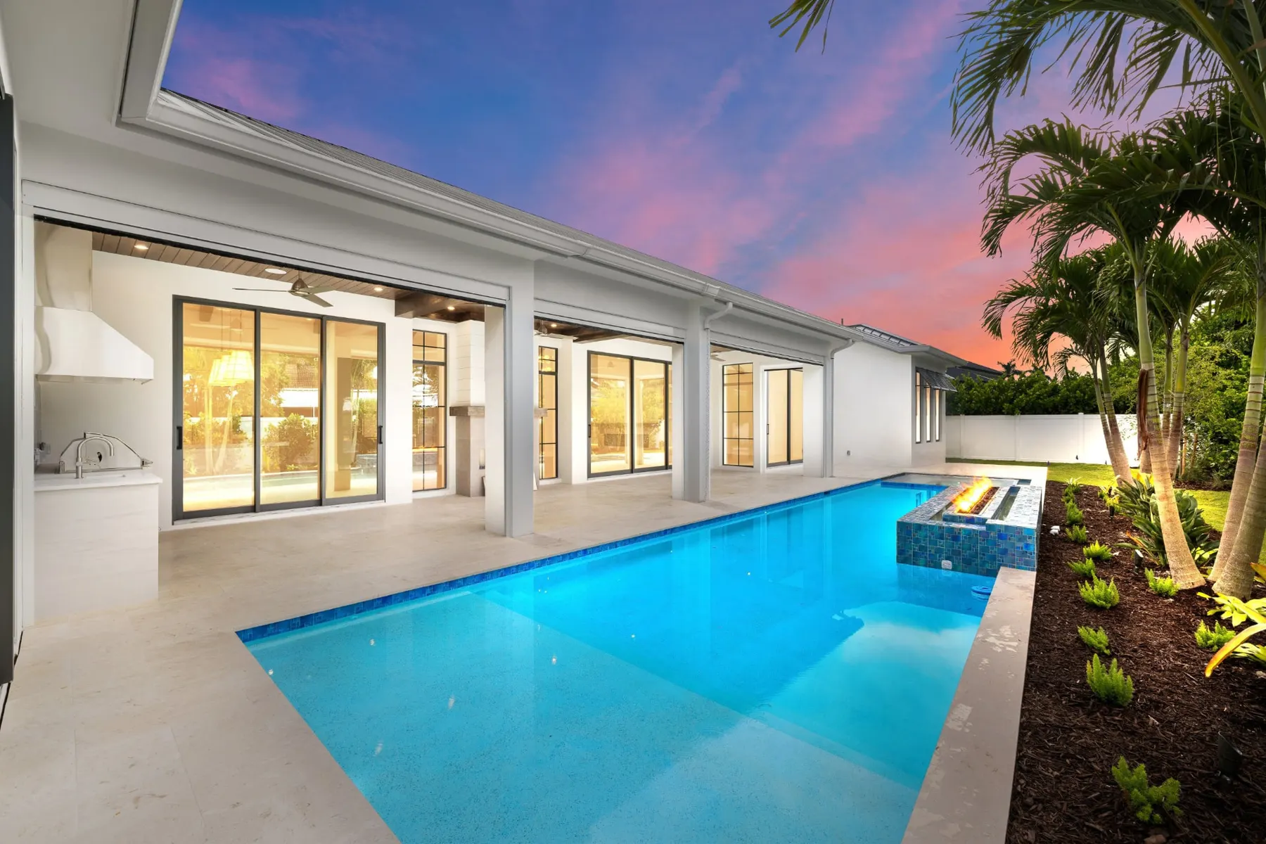 Pool from the end at dusk with the lit lanai, outdoor kitchen and palms along the right.