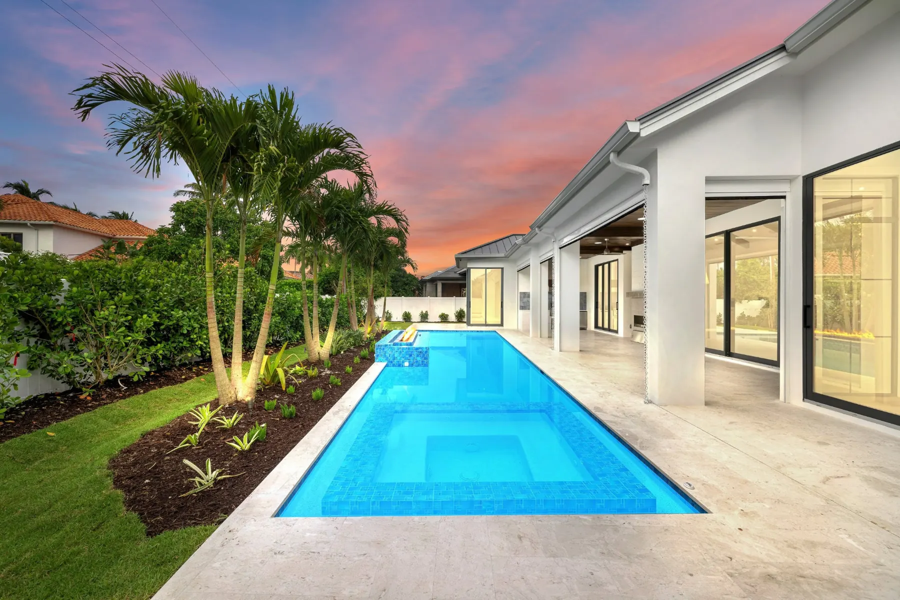 Pool and spa at dusk with the house and lit glass doors at right.