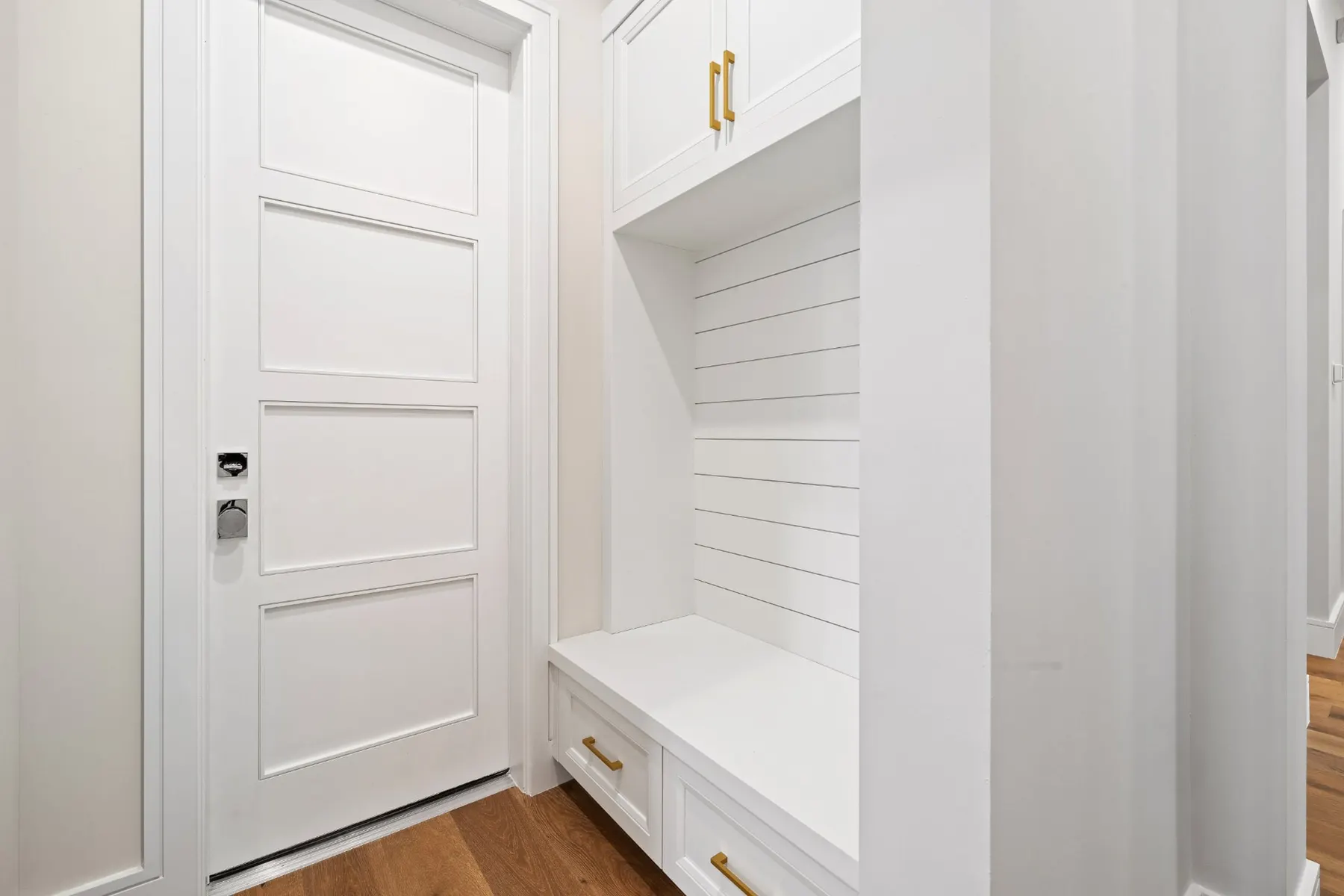 Mudroom bench with a shiplap back, upper cabinets, brass pulls and a paneled door.