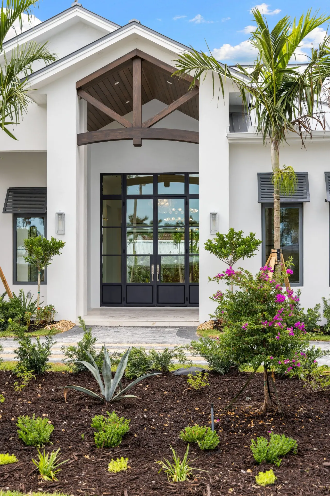 Close view of the entry in daylight, black-framed glass double doors beneath a timber truss and arched beam.