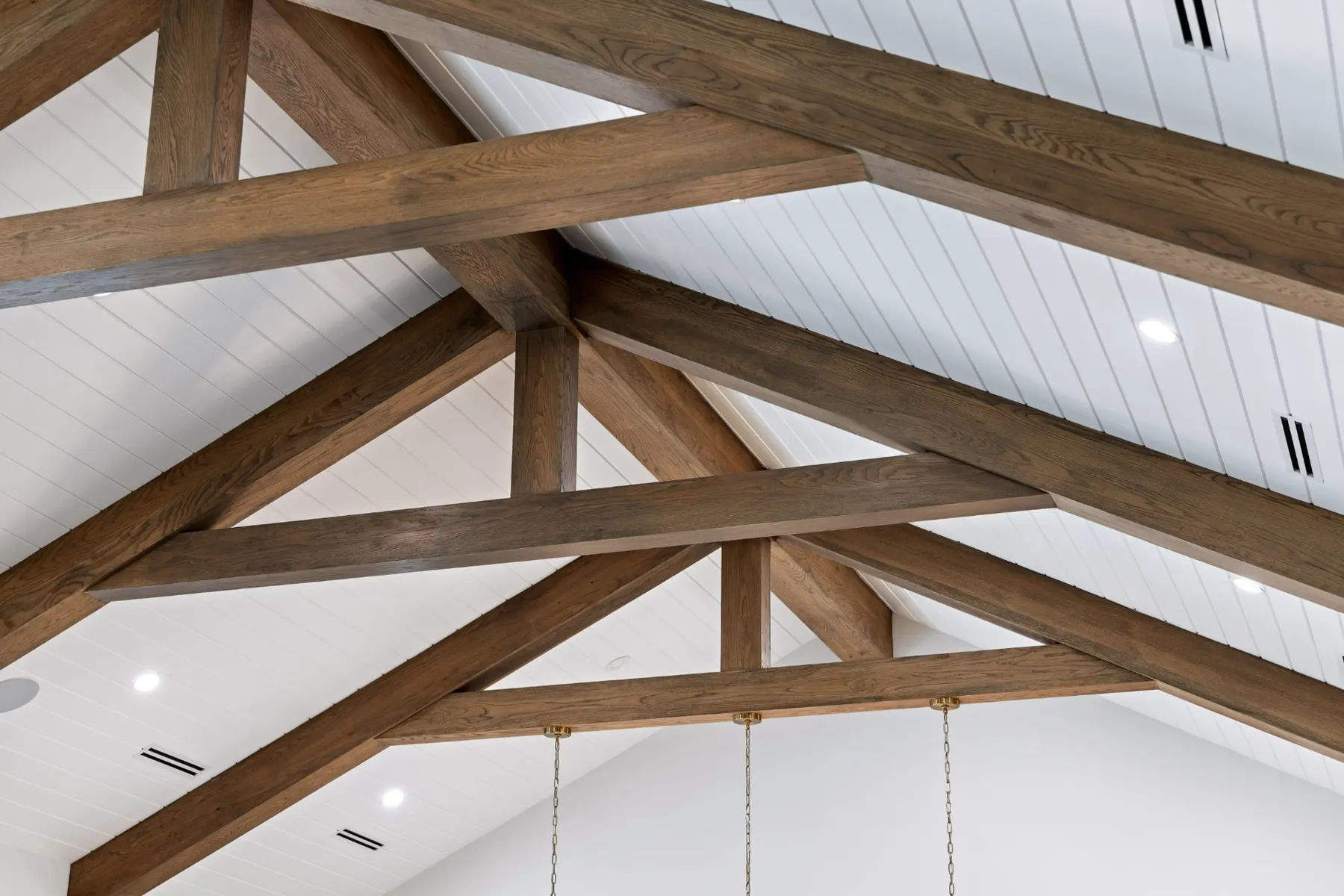 Close view of timber roof trusses over a white shiplap ceiling.