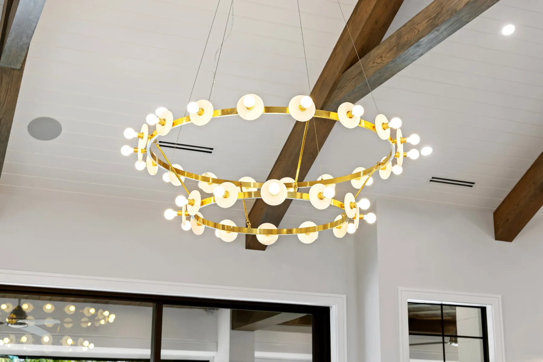 Two-tier brass ring chandelier with alabaster discs hanging below timber beams.