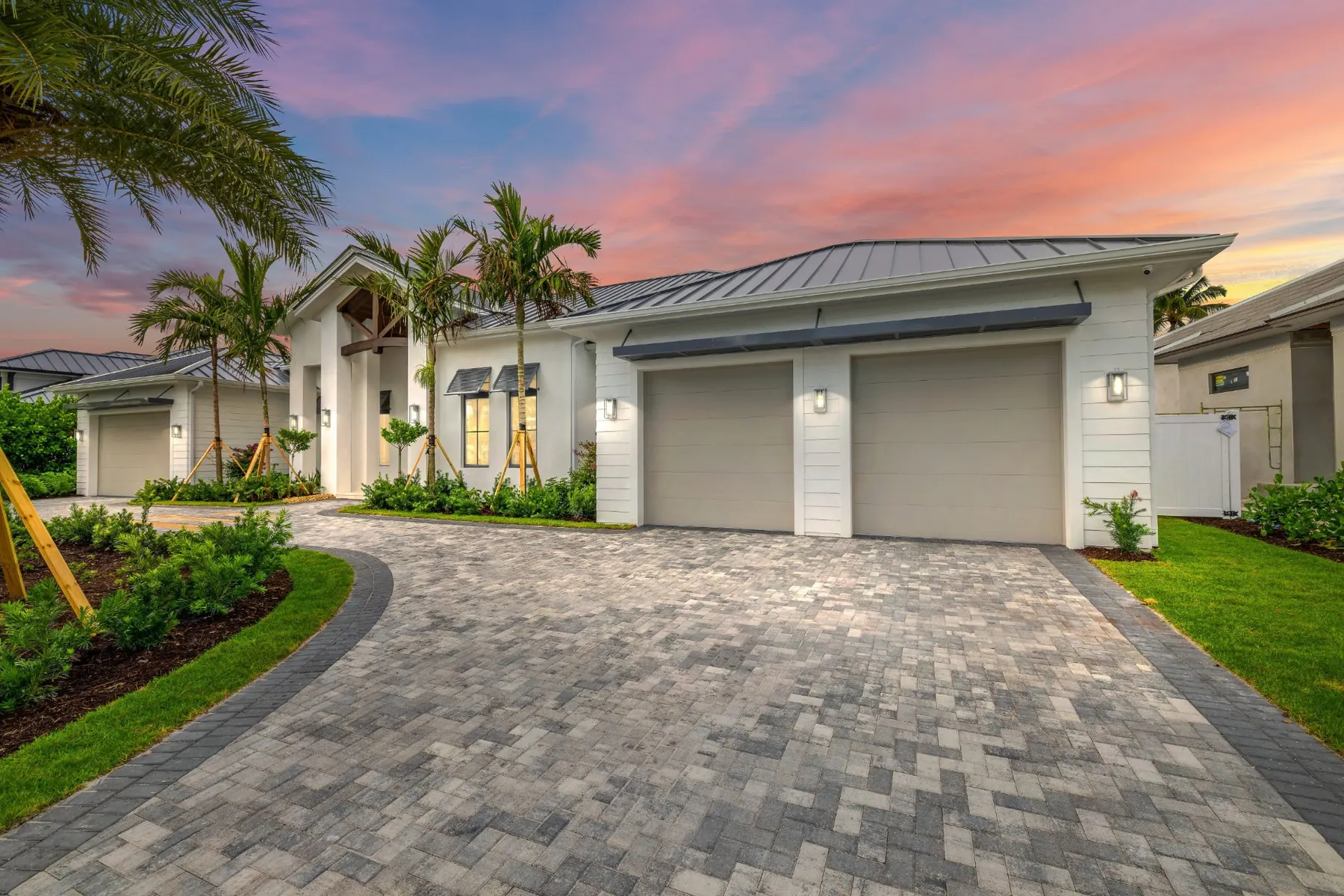 Angled view of the front at dusk with a two-car garage, a paver driveway and the entry gable beyond the palms.