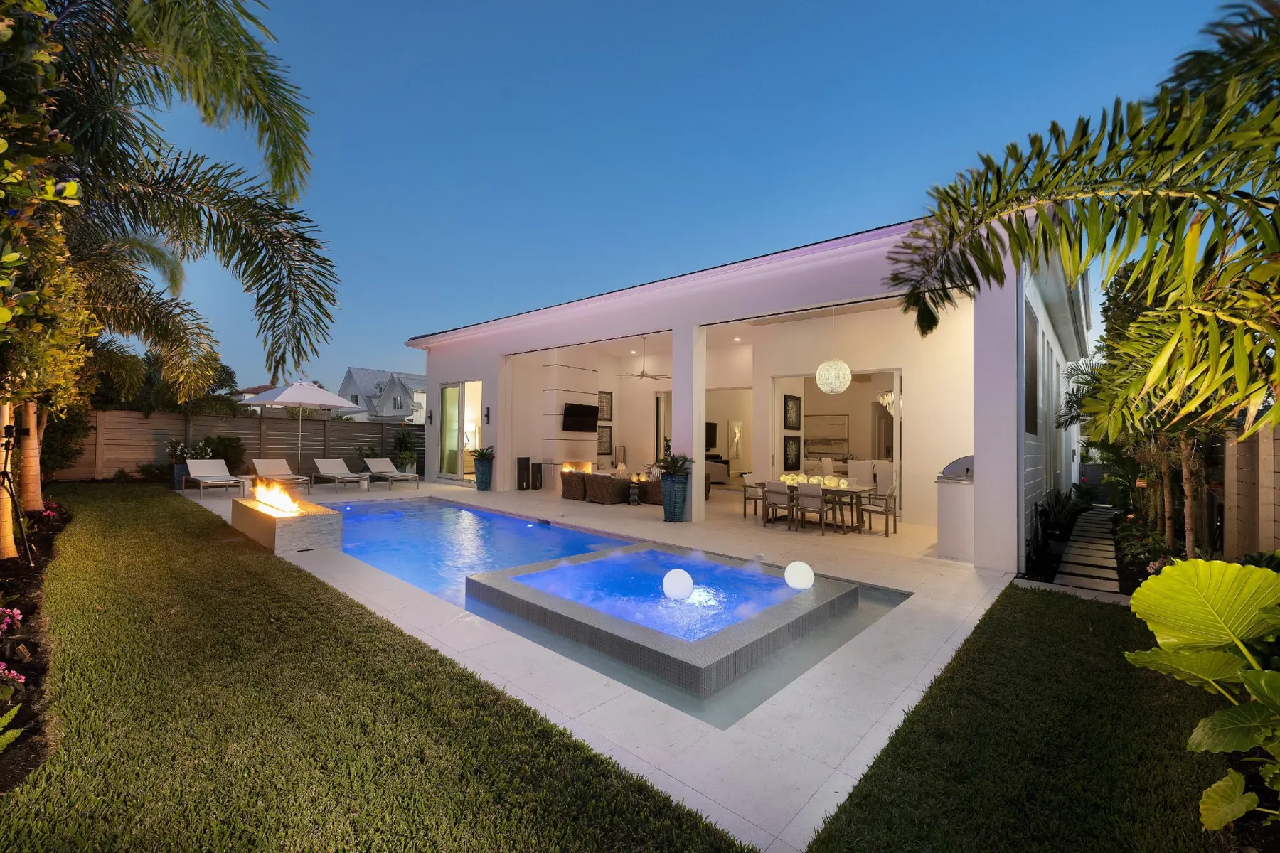 Rear of the home at dusk with a lit pool, raised spa with globe lights, a fire feature and a covered lanai.