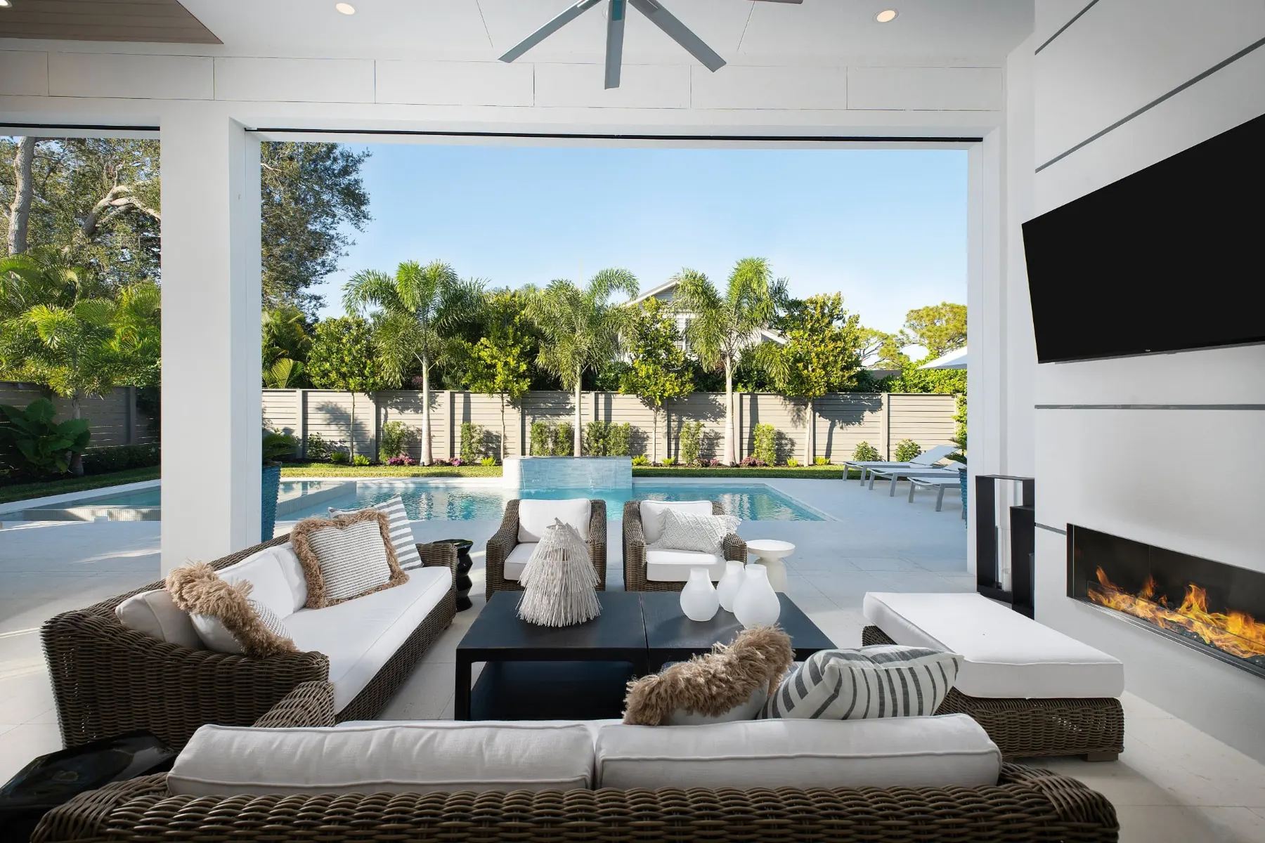 View from the lanai seating area toward the pool and water feature beyond a horizontal slat fence.