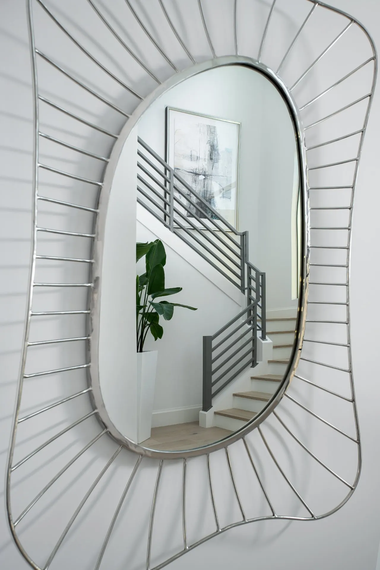 Mirror reflecting an interior stair with a horizontal metal railing and light wood treads.