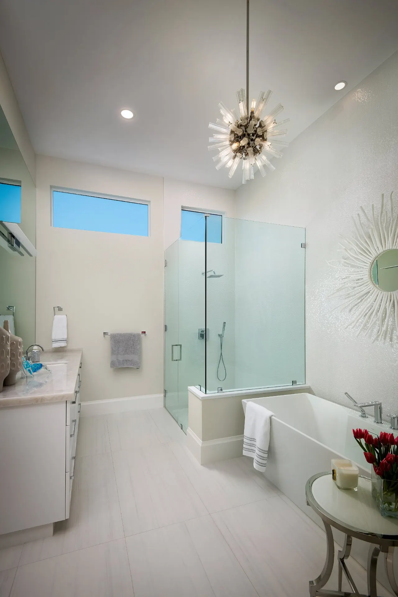 Primary bath with a glass shower, a freestanding tub and a starburst chandelier.