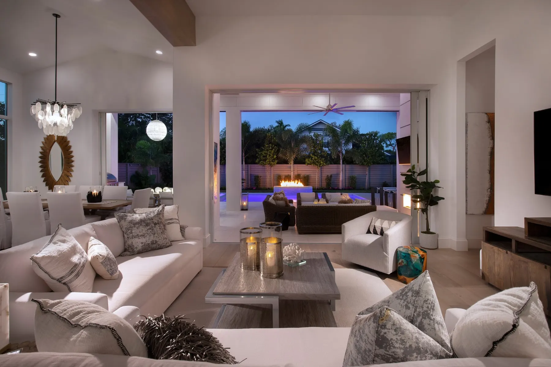 Living room at dusk looking through open sliding doors to the lit lanai, pool and fire feature.