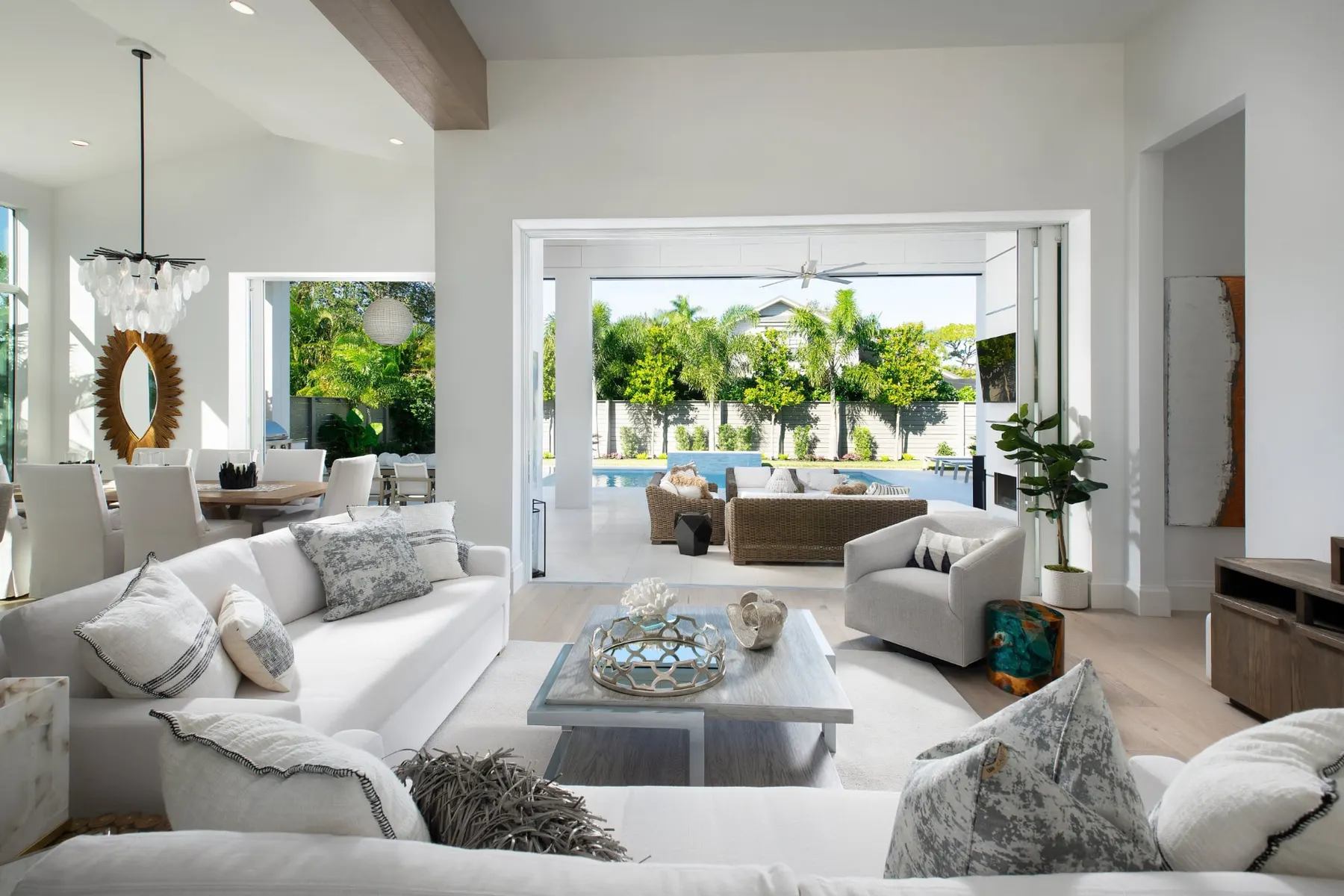 Open living room by day with white sofas, a wood-clad beam and sliding doors to the covered lanai and pool.