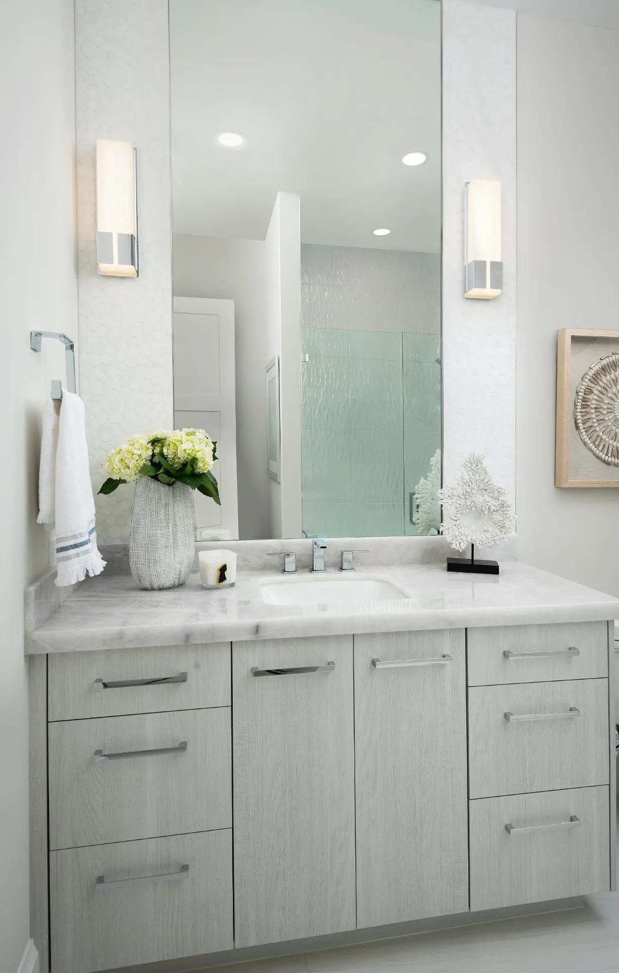 Bath vanity with a stone countertop, a tall mirror, wall sconces and flat-front cabinets.